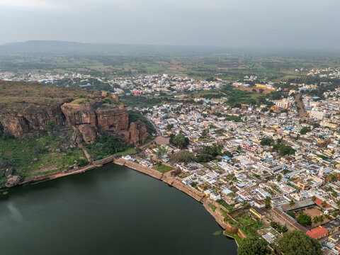 Aerial view of the ochre-red sandstone cliffs contrasting with the serene waters of Agastya Lake, nestled beside the ancient town, Badami, Karnataka, India.