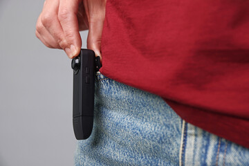 Young woman with hidden spy camera in her pocket on light grey background, closeup