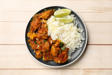 Delicious chicken tikka masala with rice, parsley and lime on light wooden table, top view