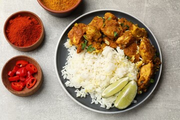 Delicious chicken tikka masala with rice, parsley, lime and spices on grey textured table, flat lay