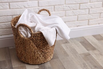 Wicker basket full of laundry on floor near white brick wall indoors. Space for text