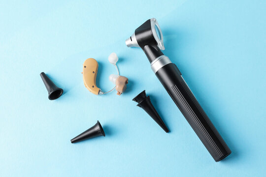 Modern otoscope, hearing aid and ear speculums on light blue background, flat lay