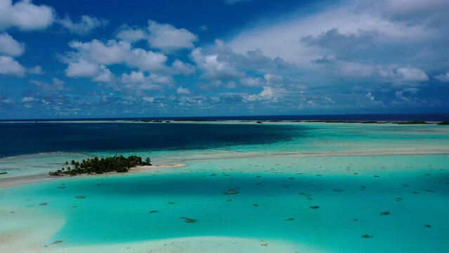 Aerial view of turquoise waters meet the deep blue sea, fringed by sandy shores and lush isles under a vast, cloud-strewn sky, Rangiroa, Tuamotu Islands, French Polynesia.