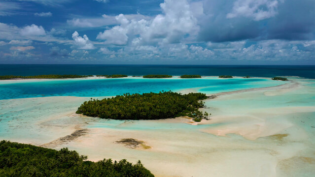 Aerial view of the atoll's shallow turquoise waters meeting the lush green islets under a vast sky, Rangiroa, Tuamotu Islands, French Polynesia.