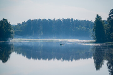 A peaceful lake captures morning fog and forest reflections as a small boat glides quietly