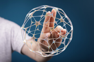 An artistic and modern image of a hand holding a glowing network sphere against a blue background,...