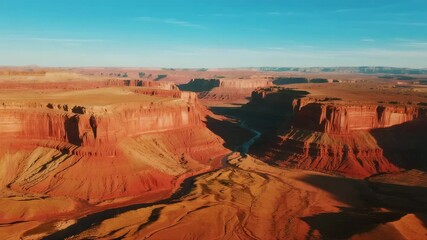 Aerial camera circles above majestic red cliffs in AlUla, sunlight flickers across layered rock textures, soft dust rises from the valley floor, creating a cinematic desert panorama.