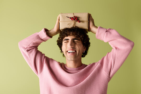 Handsome man joyfully presents a gift while dressed in trendy attire against a green background