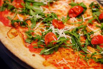 Close up Italian pizza topped with arugula and tomato