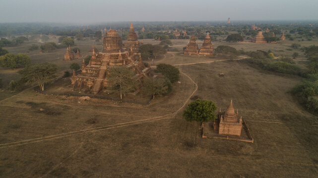 Aerial view of ancient temples and pagodas rise from the dusty plains under a soft, hazy sky, creating a serene and timeless landscape, Old Bagan, Mandalay Region, Myanmar.