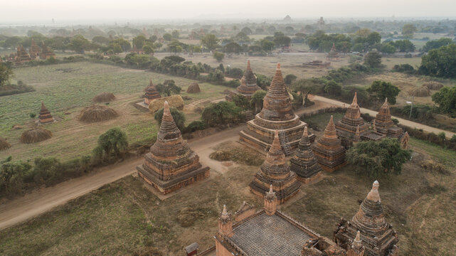 Aerial view of ancient pagodas and temples pierce through the misty landscape, their brick contrasting with the earthy tones, Old Bagan, Mandalay Region, Myanmar.