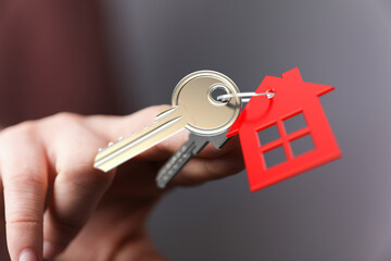 Close-up of a hand holding a key with a red house-shaped tag. A symbol of real estate,...