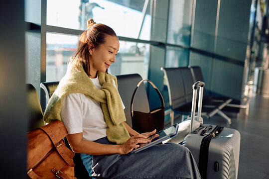 Asian woman traveling, sitting in the airport waiting area, using tablet computer and waiting for her flight - Powered by Adobe