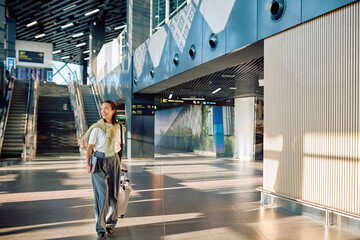 Young woman smiling, walking through a modern airport terminal, pulling a suitcase, ready for her journey