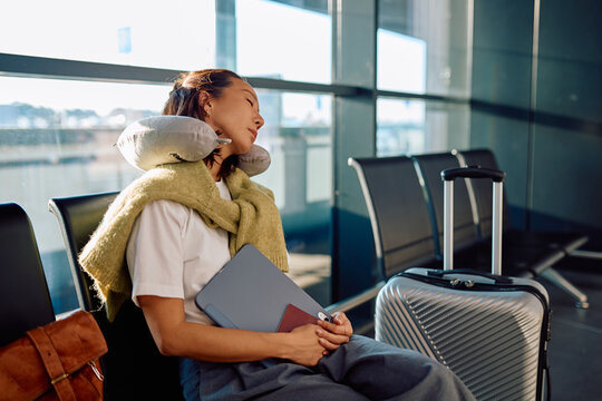 Tired woman resting comfortably with a neck pillow and luggage in an airport departure lounge, waiting for her flight