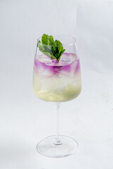 Chilled cocktail served in a tall glass, featuring ice, mint leaves, and vibrant purple flowers