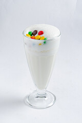 A tall glass of frothy dessert drink topped with colorful candies looks refreshing