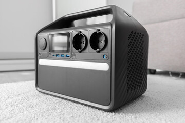 A modern portable power station with AC outlets and USB ports sits on a soft carpet indoors, providing a reliable backup energy source for home or outdoor use.