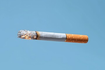 Burning Cigarette Against Clear Blue Background in Mid-Air
