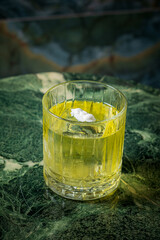 Fototapeta premium A vibrant green drink in a textured glass sits on a dark marble surface, inviting and cool