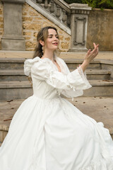 Obraz premium figure of female blonde model wearing white fantasy wedding gown. romantic sitting pose on staircase of historical fairytale castle location 