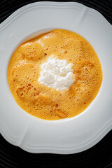 Warm, creamy soup featuring a rich orange color, topped with a fluffy white garnished swirl