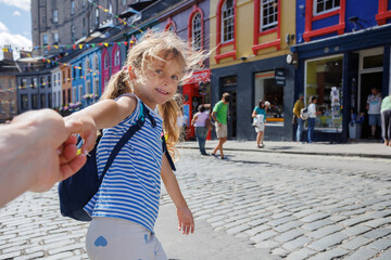 Girl traveler hold hand, walking in colorful street of Edinburgh