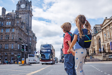 Children with backpacks cross a busy city street, hold hands