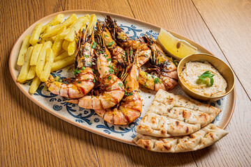 A delicious platter features grilled shrimp, crispy fries, warm flatbread, and lemon wedges