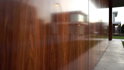 A highly polished, reflective wooden wall of a modern building, showing a blurred reflection of the exterior. - Powered by Adobe