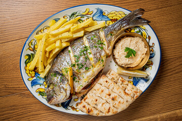 A beautifully arranged seafood dish showcasing grilled fish alongside fries, dip, and bread