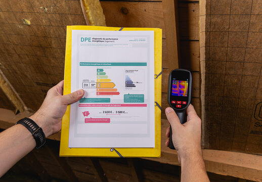 Une personne en train de remplir le formulaire du DPE avec dans une main le diagnostique de performance &eacute;nerg&eacute;tique, et dans l'autre main, une cam&eacute;ra thermique pour les fuites de chaleur. 