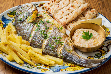 Grilled fish with crispy fries and fresh bread on a decorative platter