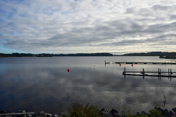 Autumn settles over Hillend Loch in Scotland, where calm waters mirror a moody, cloud-filled sky.