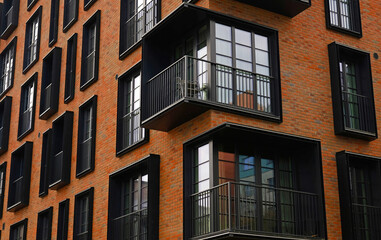 Contemporary apartment facade with warm brick cladding and black framed French windows features repeating balconies. Real estate, urban living, and property marketing.