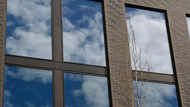 Modern brick facade with large reflective windows shows blue sky and clouds. Low angle with clean copy space. Minimalist urban style real estate, residential apartment, office building architecture - Powered by Adobe