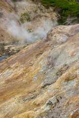 Yellow surface of soil and rocks in a mountain gorge near geothermal springs. Steam over natural hot springs. Nature of the Russian Far East. Kamchatka Territory, Russia. Beautiful natural background.