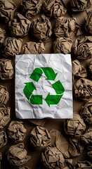 Crumpled paper balls surrounding a white sheet with a green recycle symbol in the center