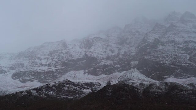 Landscape shot of dark stormy clouds above the snowy Himalayan mountain peaks during the winter storm as seen from Keylong in Lahaul and Spiti district, Himachal Pradesh, India. Scenic background.