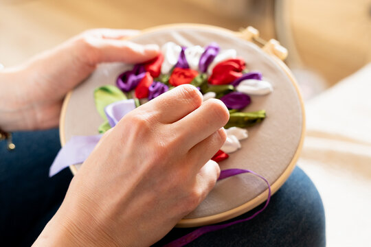 Hands creating colorful flower embroidery on a hoop during a crafting session at home in daylight