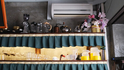 a café shelf displays glassware, coffee drippers, kettles, grinders, and jars, with green curtains framing the shelves. cafe interior design with industrial style wall