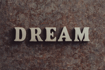 Wooden letters with the word dream on an old rusty surface, closeup, top view. Symbol of dreams and inspiration. Motivation word