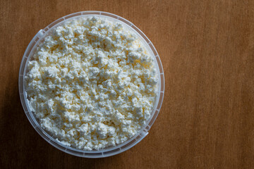 White cottage cheese or fresh milk curd in a plastic container, closeup, top view, copy space. Homemade cottage cheese texture