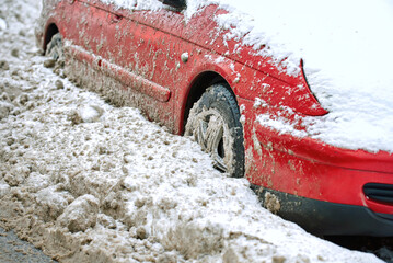 Blocked automobile surrounded by frozen slushy snow after cleanup, consequences of snow removal operations. Red automobile stuck in roadside snowdrift after municipal plow operation. Selective focus