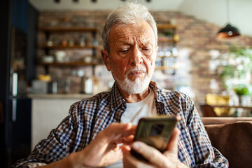 Senior man concerned while using smartphone at home