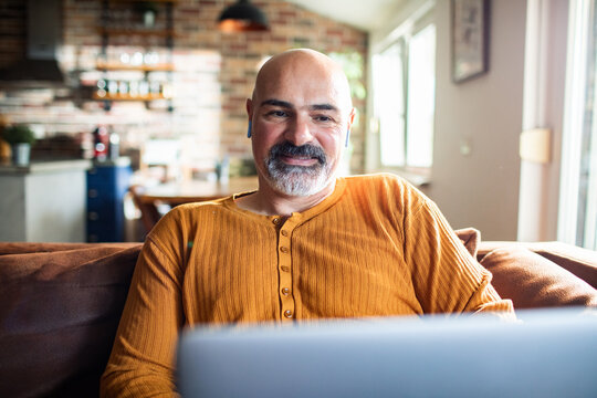 Mature man smiling with earbuds using laptop at home