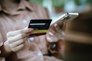 A woman holds a credit card and a smartphone, often shopping or conducting financial transactions online.