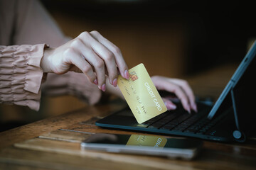 A woman holds a credit card and a smartphone, often shopping or conducting financial transactions...