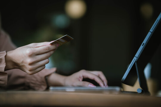 A woman holds a credit card and a smartphone, often shopping or conducting financial transactions online.