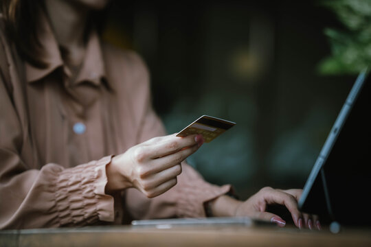 A woman holds a credit card and a smartphone, often shopping or conducting financial transactions online.